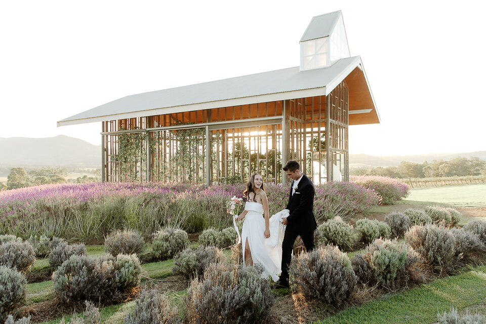 beautiful wooden chapel glowing in the sunset surrounded by purple lavendar with a bride and groom