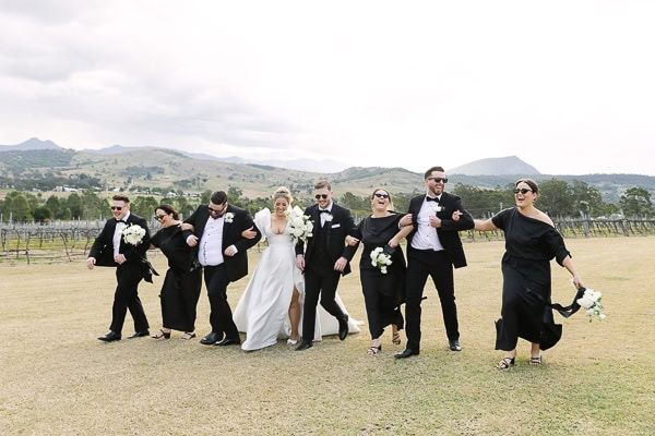 Bridal Party all in black clothes laughing and walking whilst having their arms hooked in